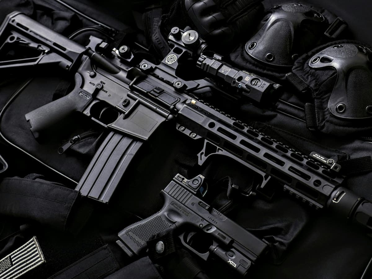 A rifle and pistol laid out with optics, mounts, and lights fitted