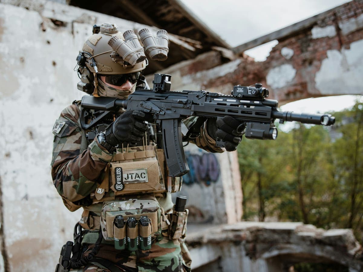 A shooter in a plate carrier and quad tube night vision, rifle shouldered